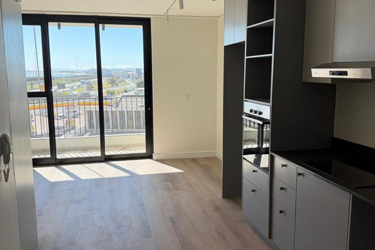 Modern open-plan kitchen and living area featuring sleek grey cabinetry, integrated appliances, laminate flooring, and large sliding doors leading to a balcony with views.