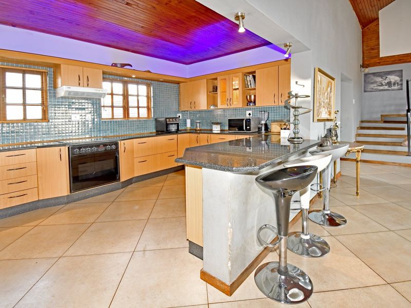 Open-plan kitchen featuring light wood cabinetry, granite countertops, a breakfast bar, and tiled flooring, seamlessly connected to the living area and staircase.
