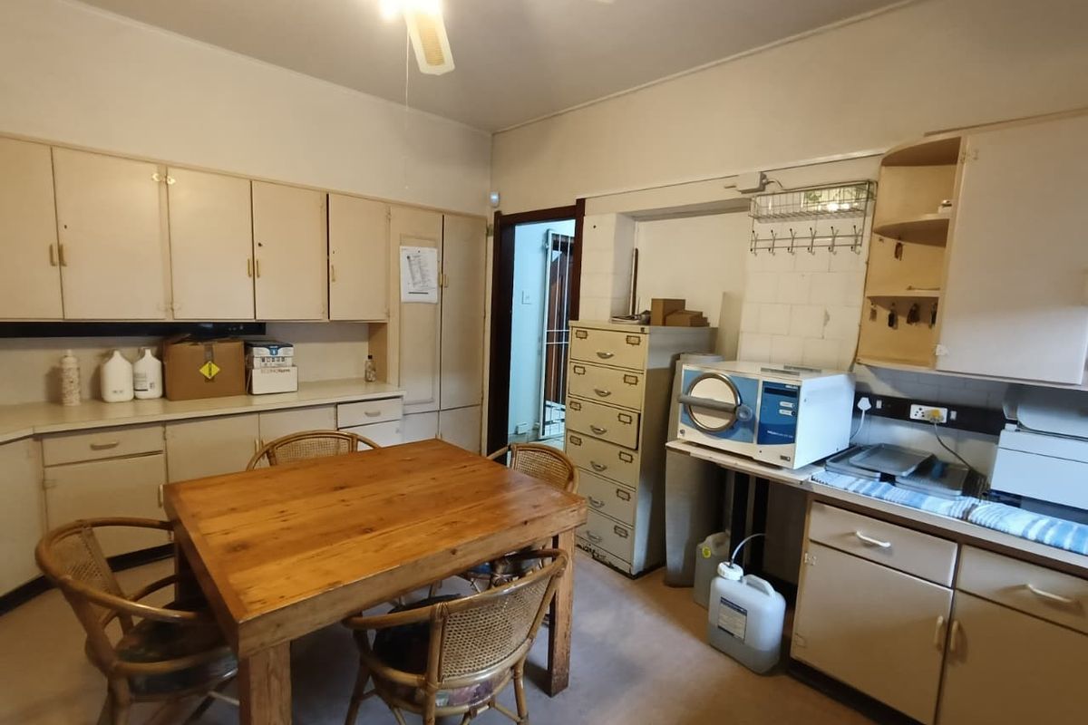 A functional kitchen area featuring extensive built-in cabinetry, a tiled backsplash, and a ceiling fan, currently utilized as a workspace.