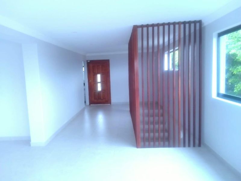 A bright, empty hallway featuring tiled flooring, a timber entrance door, and a decorative timber slat screen enclosing the staircase.