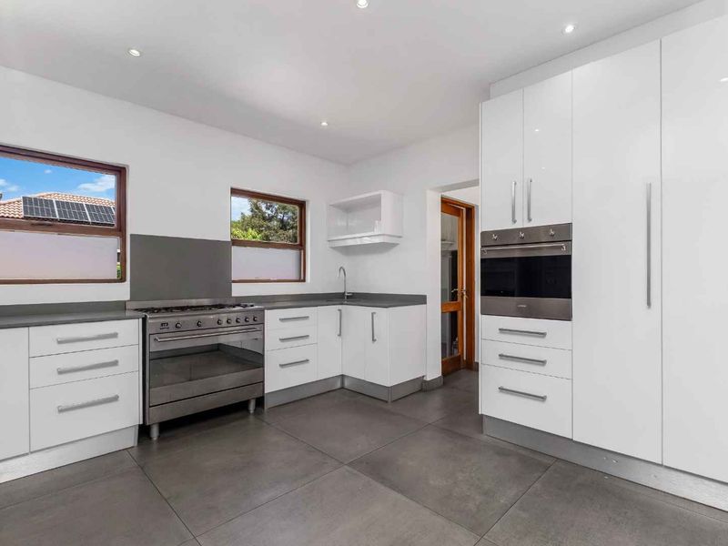 Modern kitchen featuring white cabinetry, stainless steel built-in oven, gas stove, and large format floor tiles with ample natural light.
