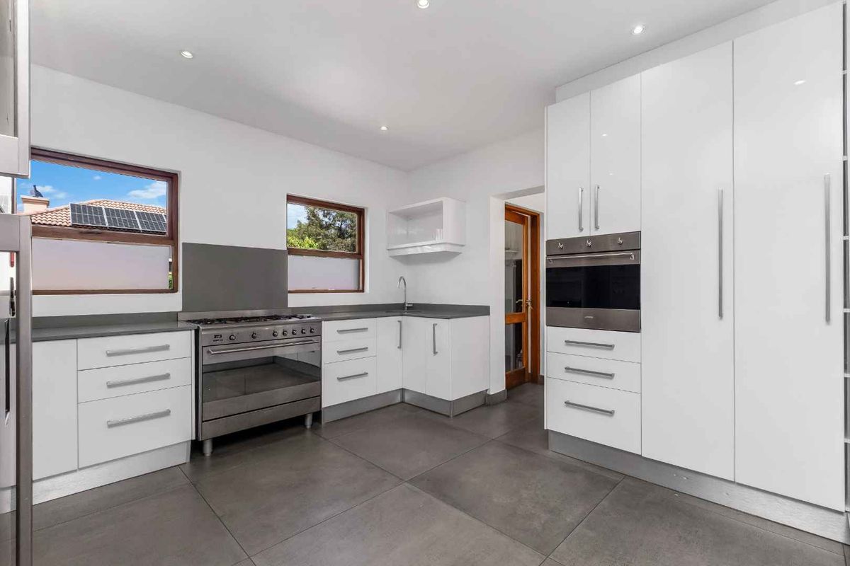 Modern kitchen featuring white cabinetry, stainless steel built-in oven, gas stove, and large format floor tiles with ample natural light.