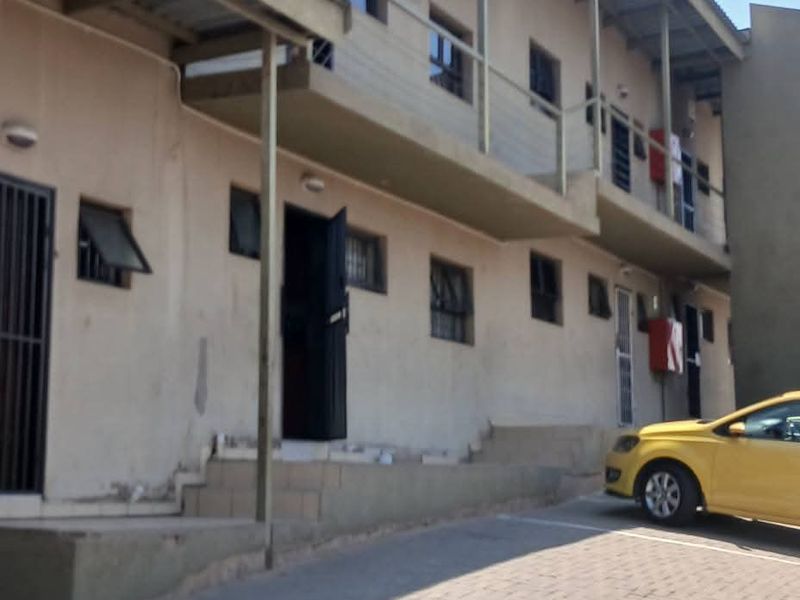 Exterior view of a multi-story apartment building featuring a paved driveway, balcony access, and security fixtures.