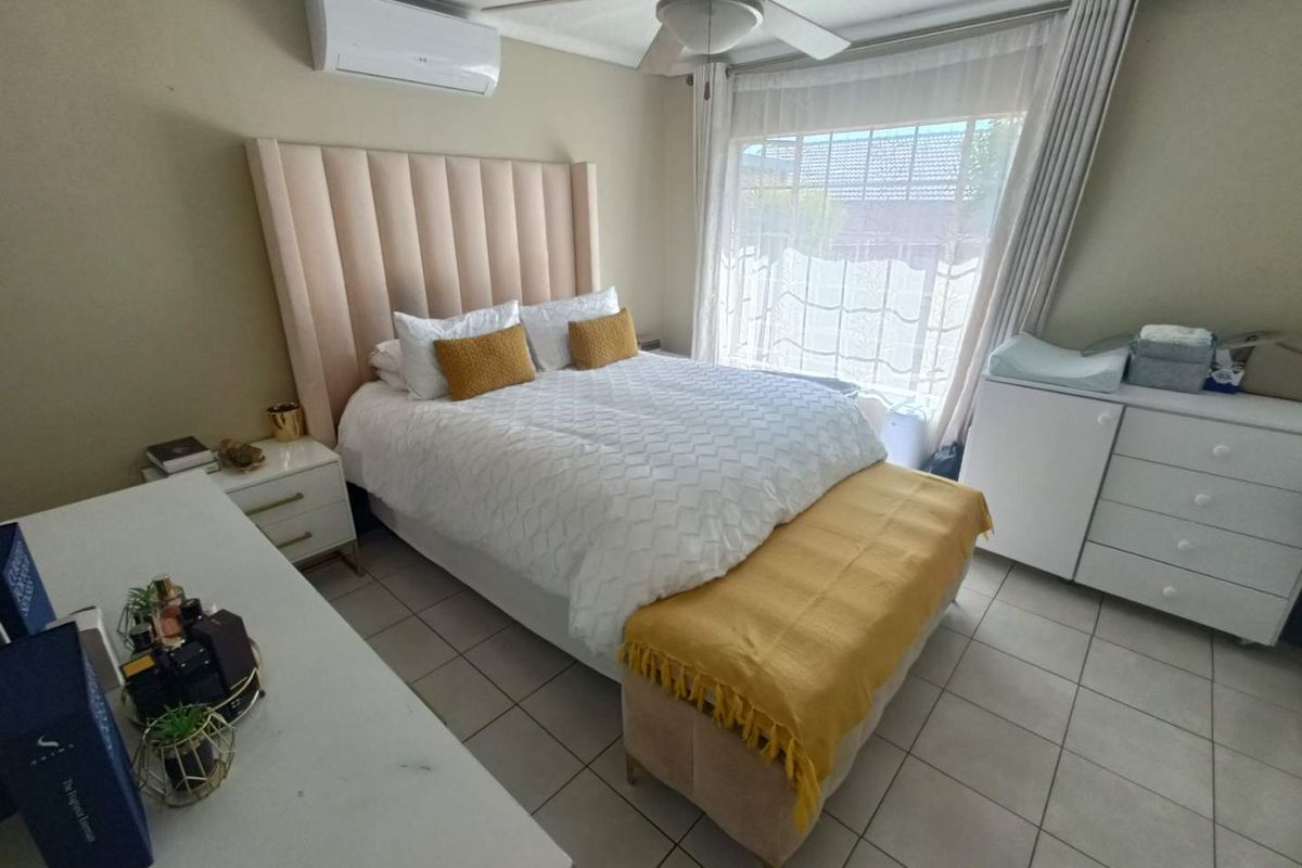 A well-maintained bedroom featuring tiled flooring, a ceiling fan, and a wall-mounted split-system air conditioner for climate control.