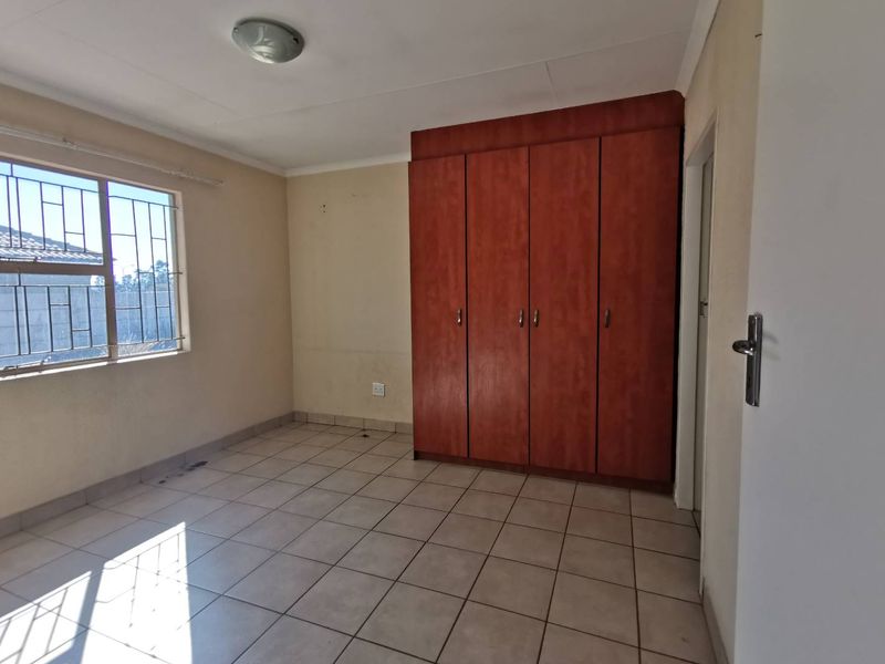 A vacant bedroom featuring tiled flooring, built-in wooden cupboards, and security bars on the window, offering a blank canvas for personalization.
