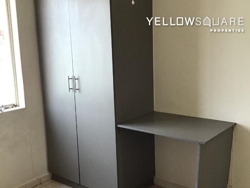 A bedroom featuring a built-in wardrobe and integrated desk, finished with tiled flooring and neutral wall tones.