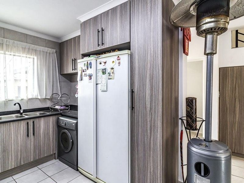 A functional kitchen featuring wood-look laminate cabinetry, granite countertops, and tiled flooring, with integrated space for laundry appliances.