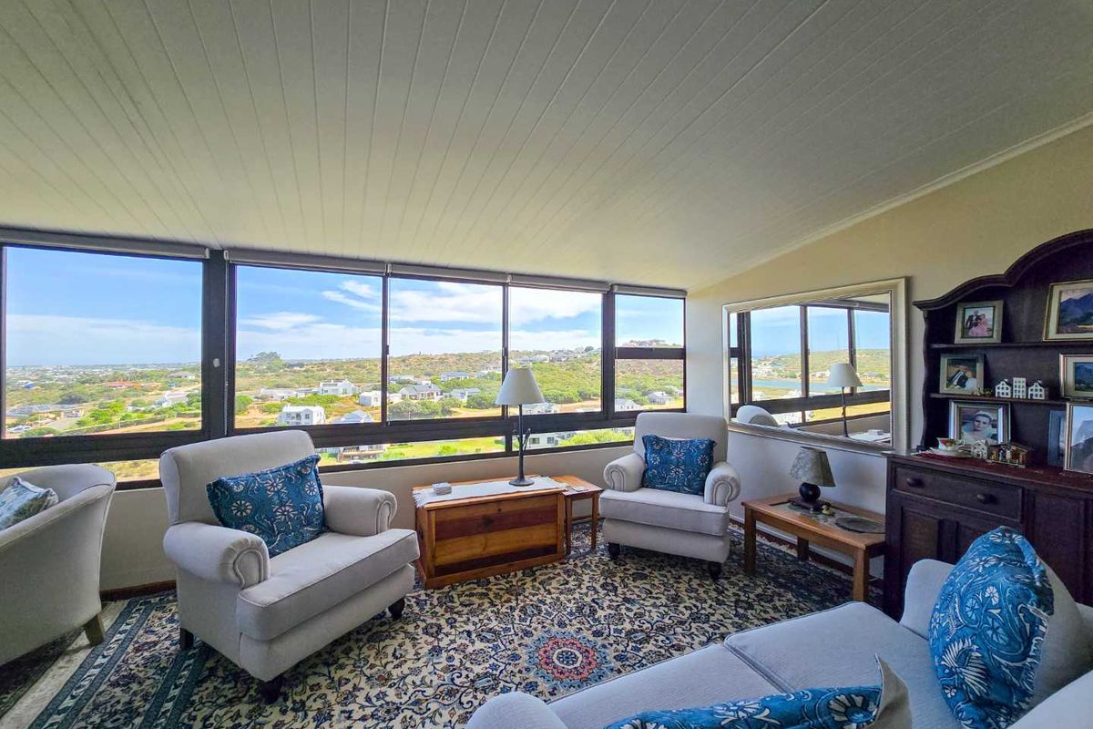 A bright living area featuring expansive windows with panoramic coastal views, wood-paneled ceiling, and large wall-mounted mirror.