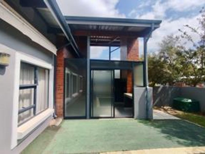 A covered outdoor patio area featuring brick accents, sliding glass doors, and paved flooring, providing a functional transition space between the interior and garden.