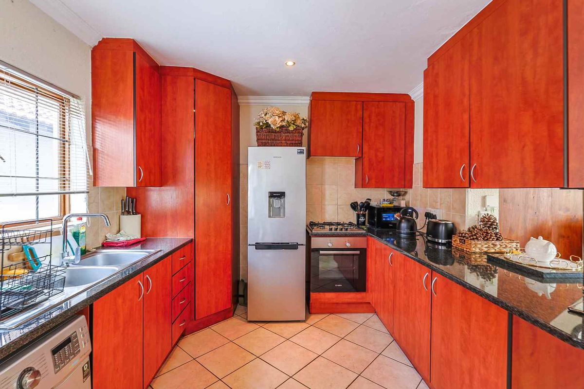 A functional kitchen featuring cherry-wood cabinetry, granite countertops, a built-in oven with gas hob, and tiled flooring.