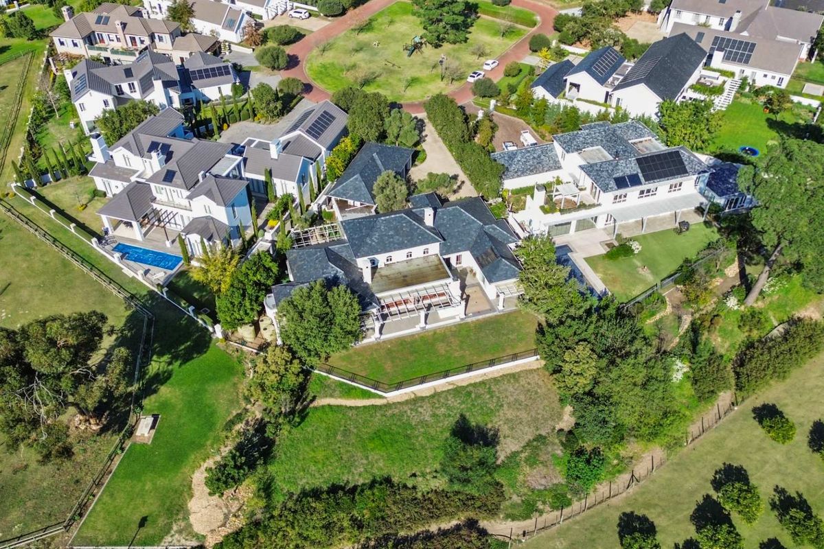 Aerial view of a residential estate featuring multiple homes with pitched roofs, solar panels, swimming pools, and expansive landscaped grounds.