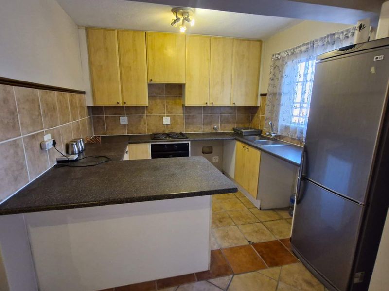 A functional kitchen featuring wooden cabinetry, dark laminate countertops, tiled backsplash, built-in oven, hob, and a double sink with tiled flooring.