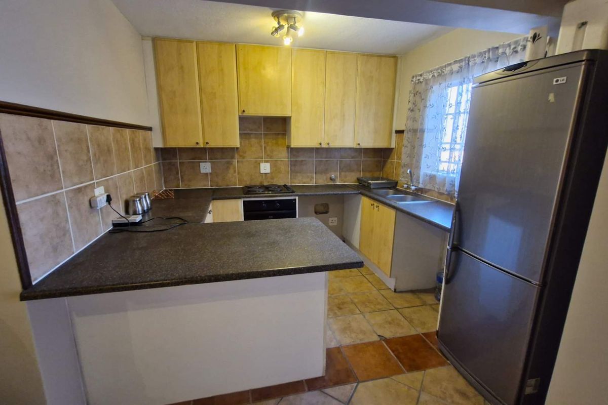 A functional kitchen featuring wooden cabinetry, dark laminate countertops, tiled backsplash, built-in oven, hob, and a double sink with tiled flooring.
