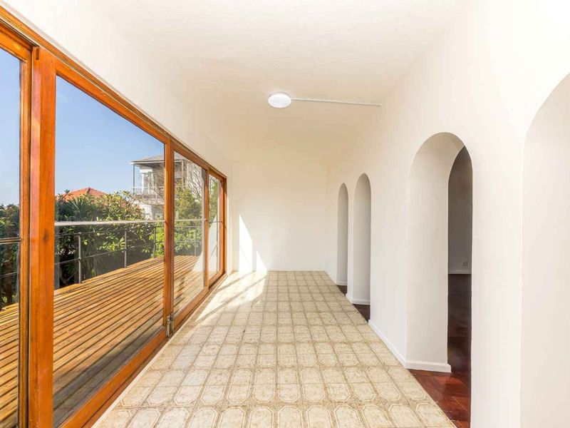 A bright, covered balcony featuring timber decking, large sliding glass doors, and distinctive arched architectural details, offering a seamless transition to outdoor space.