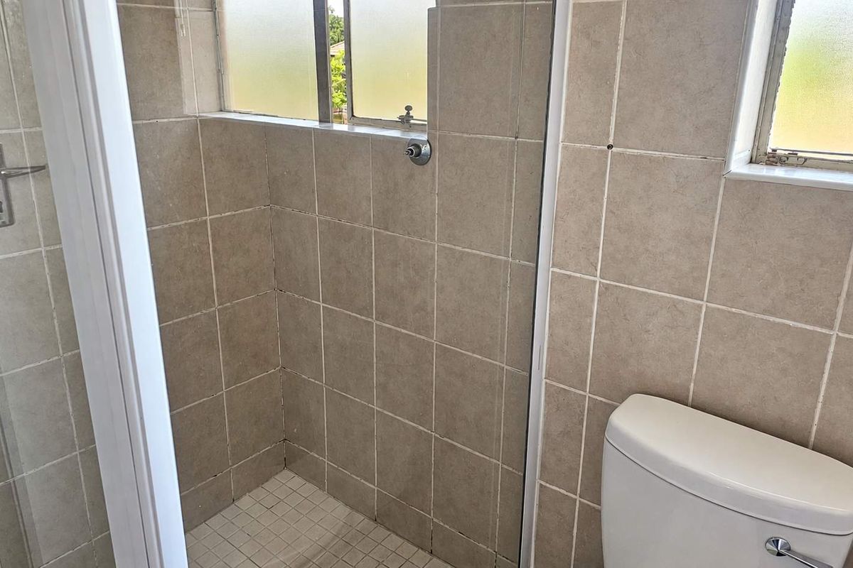 A functional bathroom featuring a shower enclosure with tiled walls and a standard toilet, finished with neutral ceramic tiling throughout.