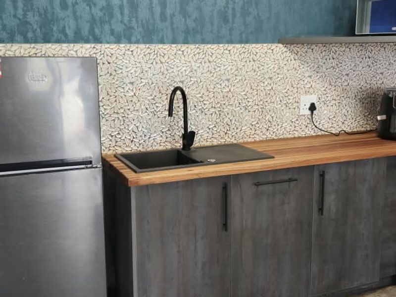 A modern kitchen area featuring a wooden countertop, black sink with matching tap, textured cabinetry, and a decorative tiled backsplash.
