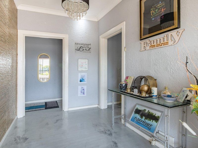 A bright hallway featuring a textured accent wall, decorative chandelier, and neutral wall tones, providing access to adjacent rooms.