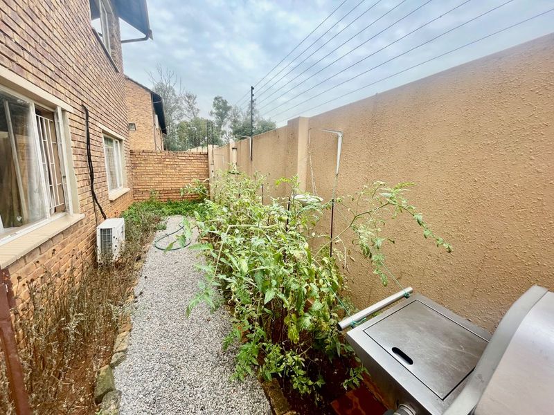 A narrow rear exterior side passage featuring a gravel pathway, brick boundary wall with electric fencing, and an external air conditioning unit.