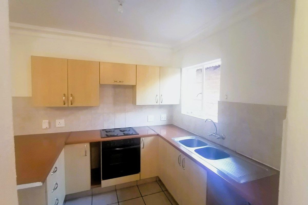 A functional kitchen featuring laminate countertops, built-in oven, electric hob, and double bowl sink, with tiled flooring and ample cabinetry throughout.