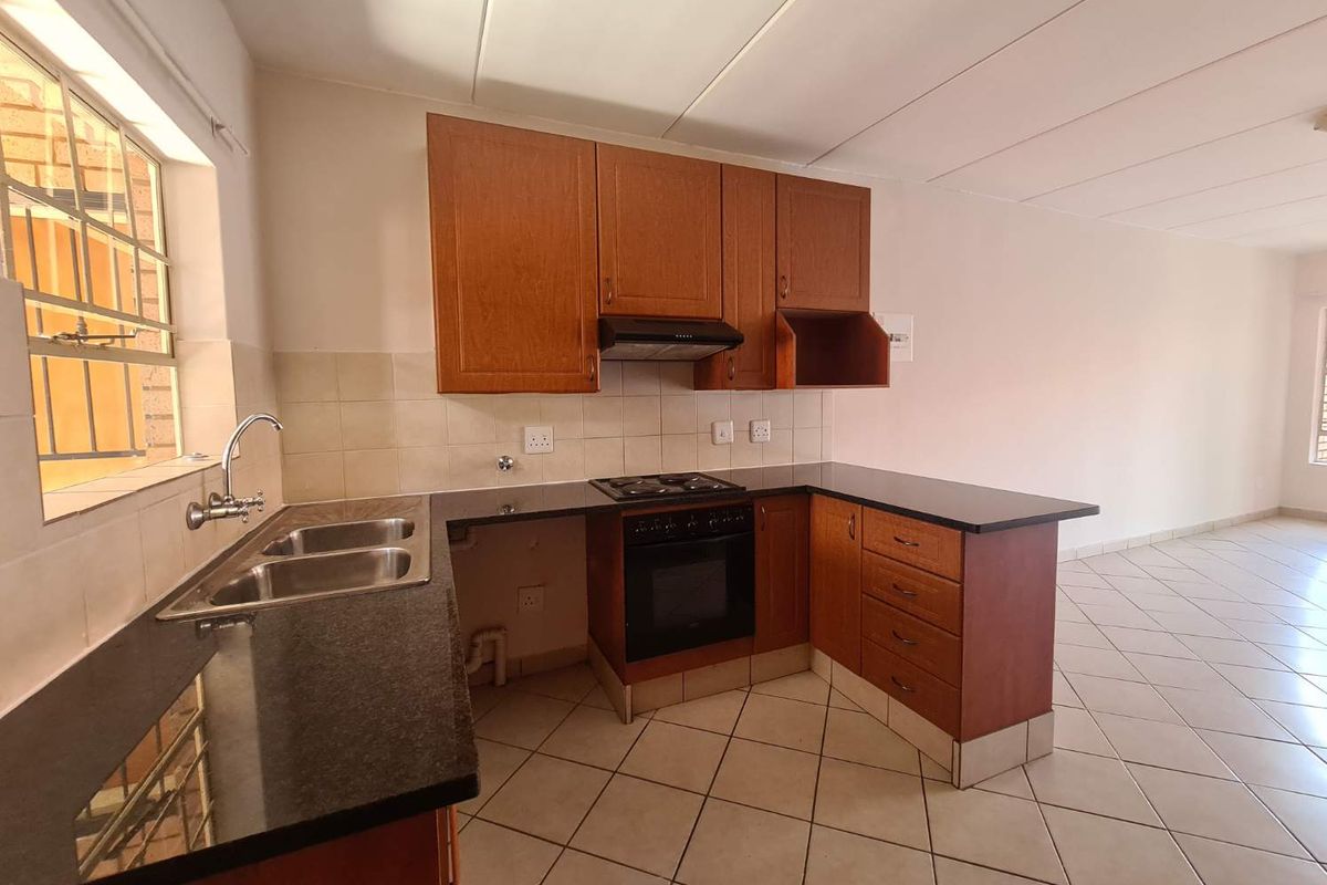 A functional kitchen featuring laminate cabinetry, granite countertops, a built-in oven with hob, and tiled flooring in an open-plan layout.
