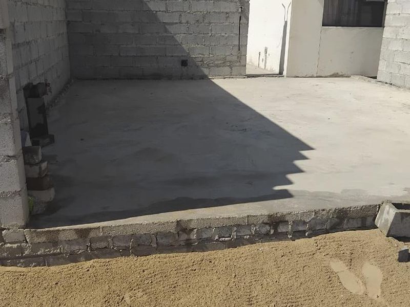 An unfinished rear outdoor area featuring a concrete slab patio and exposed cinder block boundary walls, awaiting landscaping and final finishes.