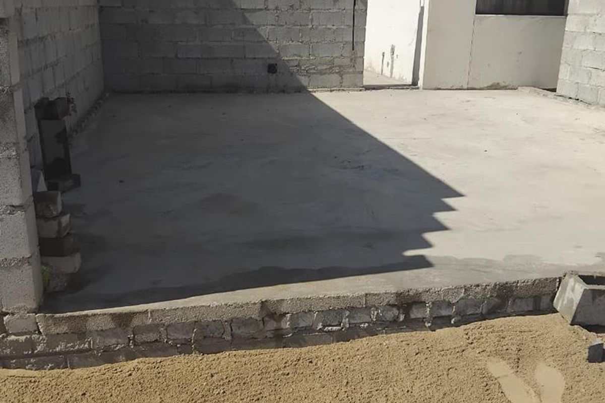 An unfinished rear outdoor area featuring a concrete slab patio and exposed cinder block boundary walls, awaiting landscaping and final finishes.