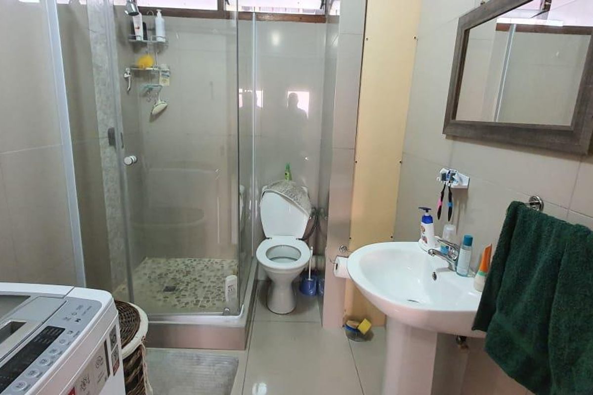 A functional bathroom featuring a pedestal basin, a glass-enclosed shower, and a toilet, with neutral wall and floor tiling throughout.