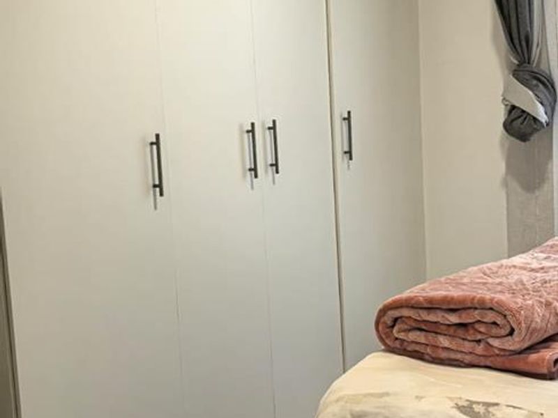 A bedroom featuring neutral tiled flooring and floor-to-ceiling built-in cupboards with modern handles.