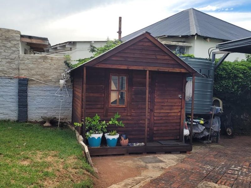 A wooden garden shed situated in the rear yard, featuring a brick paved driveway and an adjacent water storage tank.