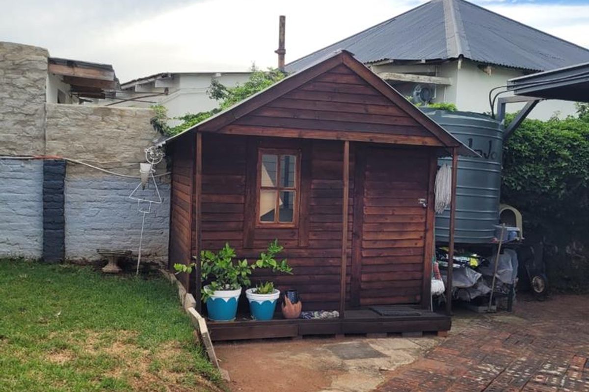 A wooden garden shed situated in the rear yard, featuring a brick paved driveway and an adjacent water storage tank.