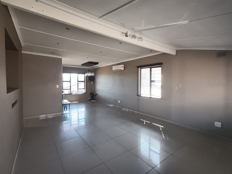 Spacious, open-plan living area featuring neutral tiled flooring, recessed lighting, and a wall-mounted air conditioning unit, offering a versatile blank canvas.