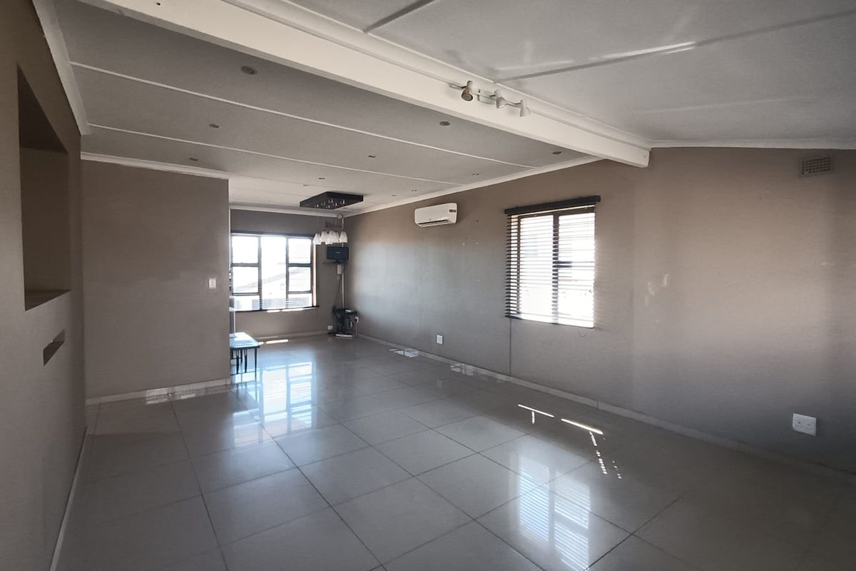 Spacious, open-plan living area featuring neutral tiled flooring, recessed lighting, and a wall-mounted air conditioning unit, offering a versatile blank canvas.