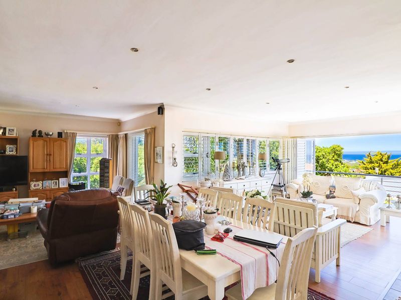Spacious open-plan living and dining area featuring laminate flooring, recessed lighting, and large sliding doors opening to a scenic coastal view.