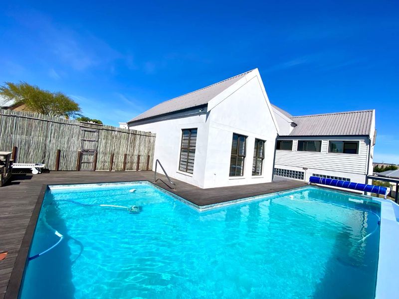 A well-maintained outdoor pool area featuring timber decking, a swimming pool with a cover, and a modern white building facade.