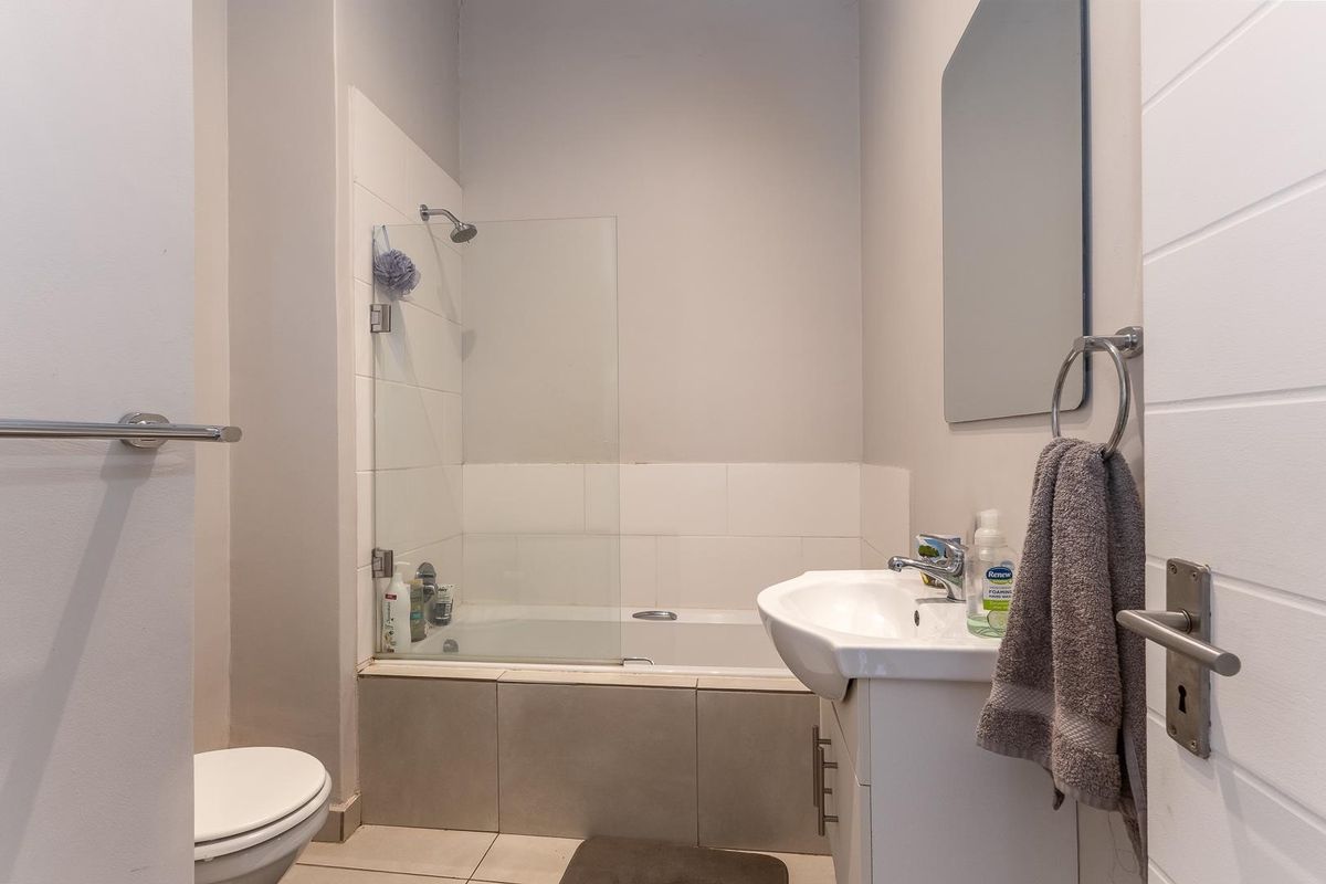 A clean and functional bathroom featuring a bathtub with a glass shower screen, a vanity basin, and a toilet with neutral tiled finishes.