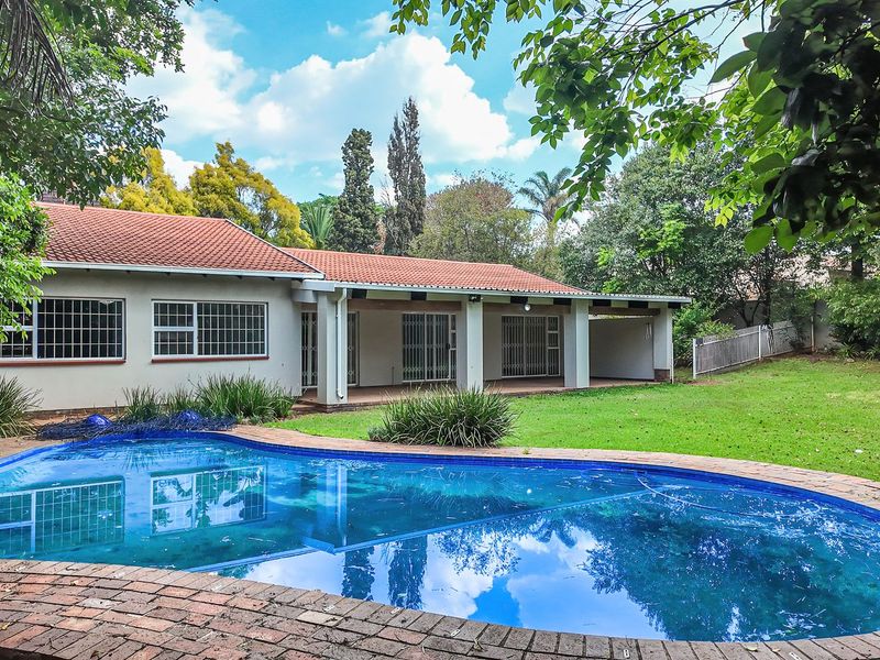 A spacious backyard featuring a swimming pool with brick coping, a well-maintained lawn, and a covered patio area attached to the main house.