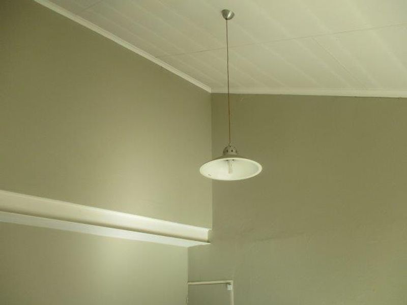 A view of a room corner featuring a pendant light fixture, coving, and skirting boards against plain painted walls.