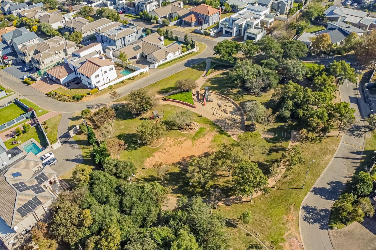 An aerial view of a residential estate featuring a central park area with mature trees, walking paths, and a playground.