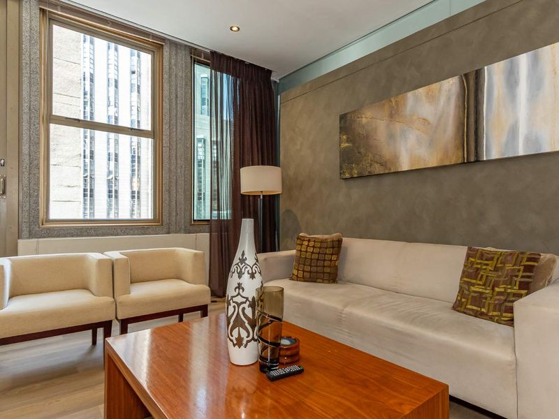 A well-maintained living room featuring a textured feature wall, recessed downlighting, and large windows providing ample natural light.