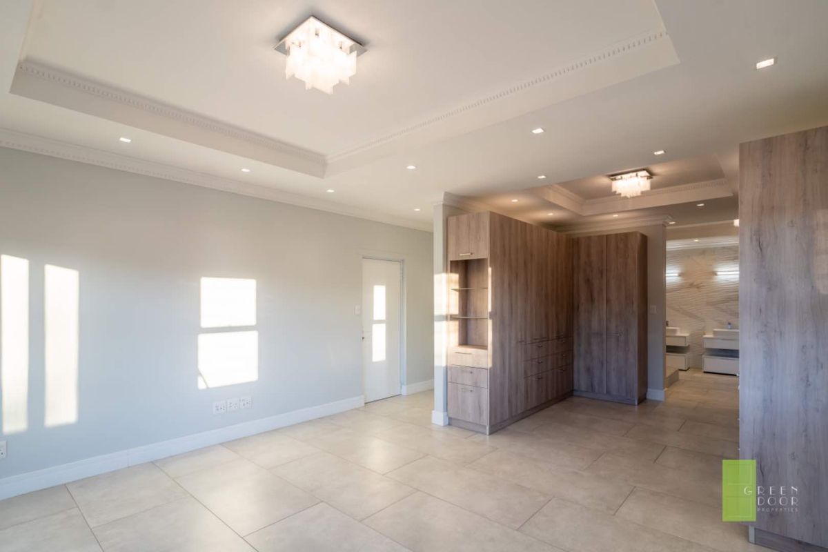 Spacious bedroom featuring built-in wooden cabinetry, recessed ceiling lighting, and tiled flooring, with an open-plan layout leading to an en-suite bathroom area.
