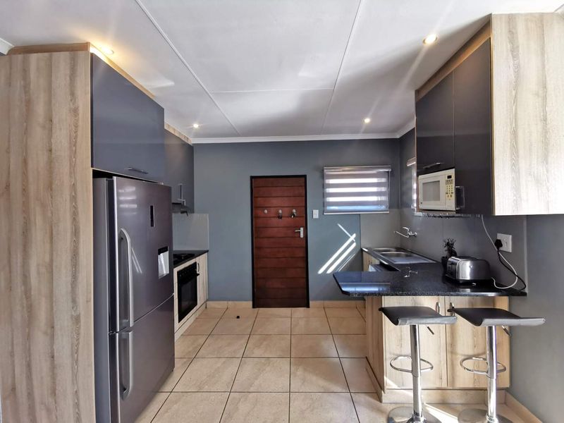Modern kitchen featuring sleek two-tone cabinetry, granite countertops, built-in oven and hob, and tiled flooring, offering a functional and contemporary cooking space.