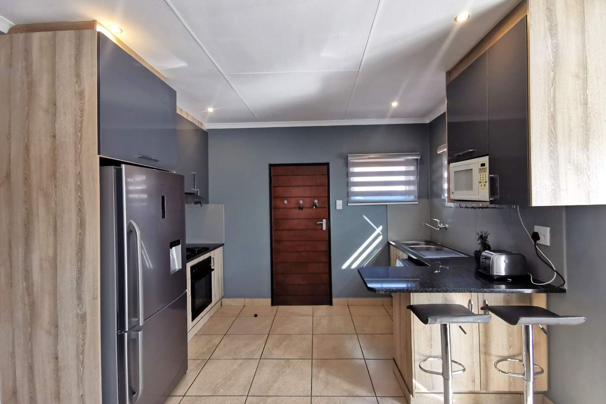 Modern kitchen featuring sleek two-tone cabinetry, granite countertops, built-in oven and hob, and tiled flooring, offering a functional and contemporary cooking space.