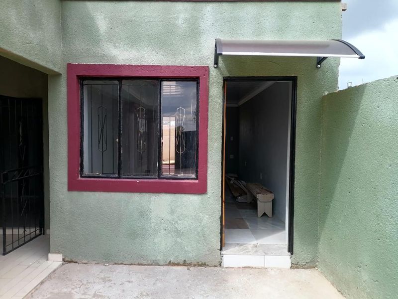 Rear exterior view showing a textured wall, security-barred window, and a small entrance awning over the doorway.