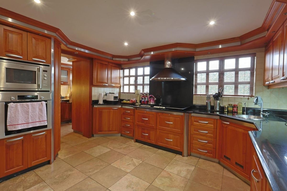 A spacious kitchen featuring warm-toned wooden cabinetry, black granite countertops, integrated stainless steel appliances, and tiled flooring with recessed ceiling lighting.