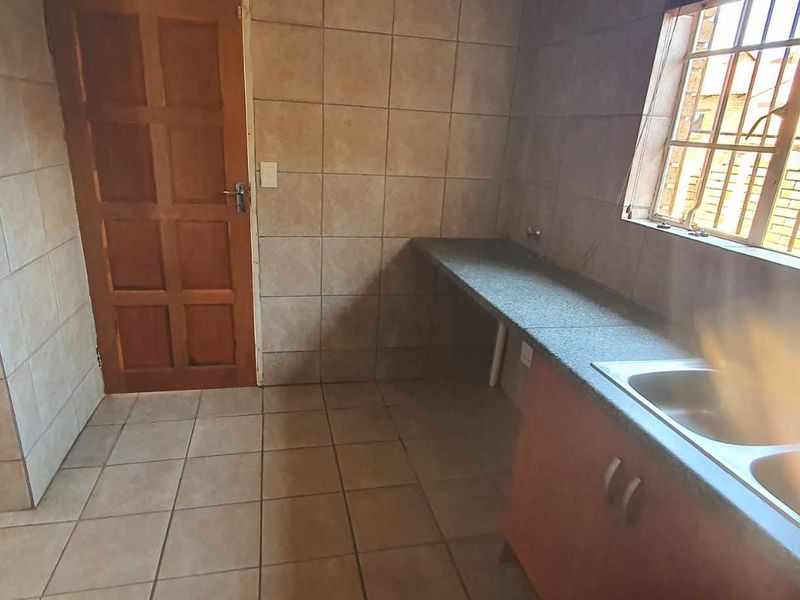 A functional kitchen area featuring tiled walls and flooring, granite countertops, and a double bowl sink, with security bars installed on the windows.