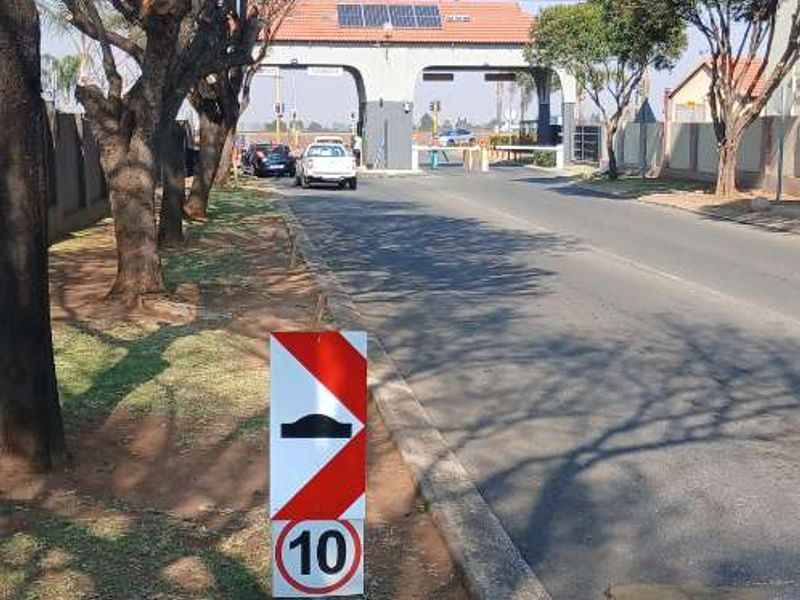 A view of the residential complex entrance featuring a security gatehouse with solar panels and a paved access road.