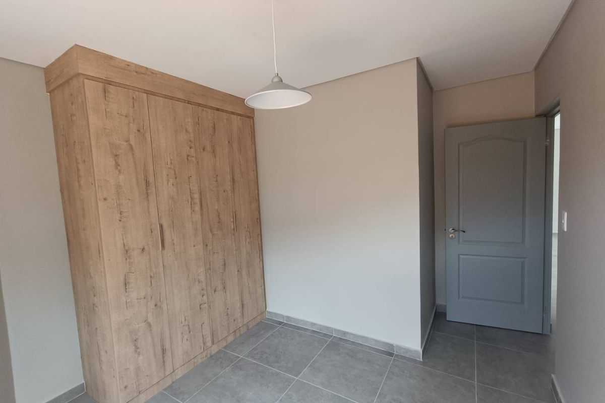 A clean, modern bedroom featuring built-in wood-grain cabinetry, neutral wall tones, and contemporary grey floor tiling.