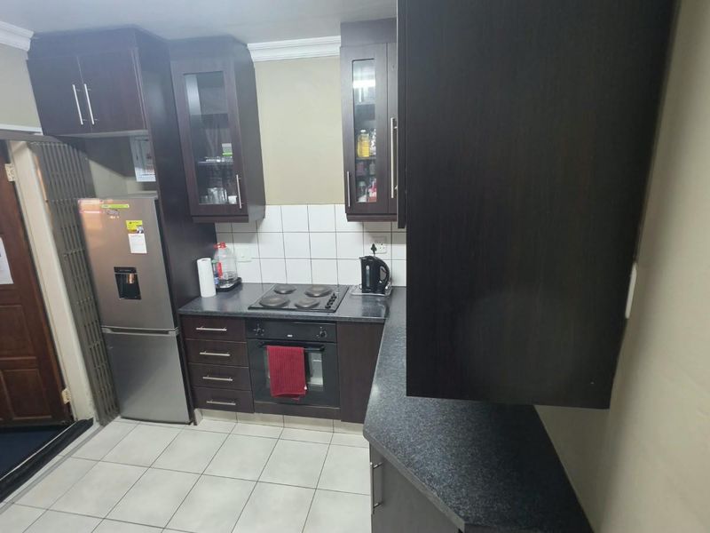 A functional kitchen featuring dark wood cabinetry, laminate countertops, built-in oven, electric hob, and tiled flooring.