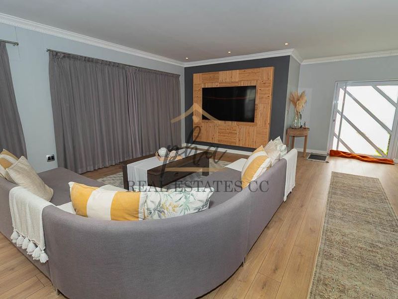 A well-maintained living room featuring laminate flooring, recessed lighting, and a decorative feature wall with integrated media space.