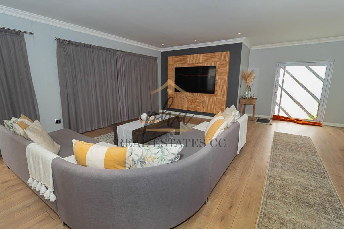 A well-maintained living room featuring laminate flooring, recessed lighting, and a decorative feature wall with integrated media space.